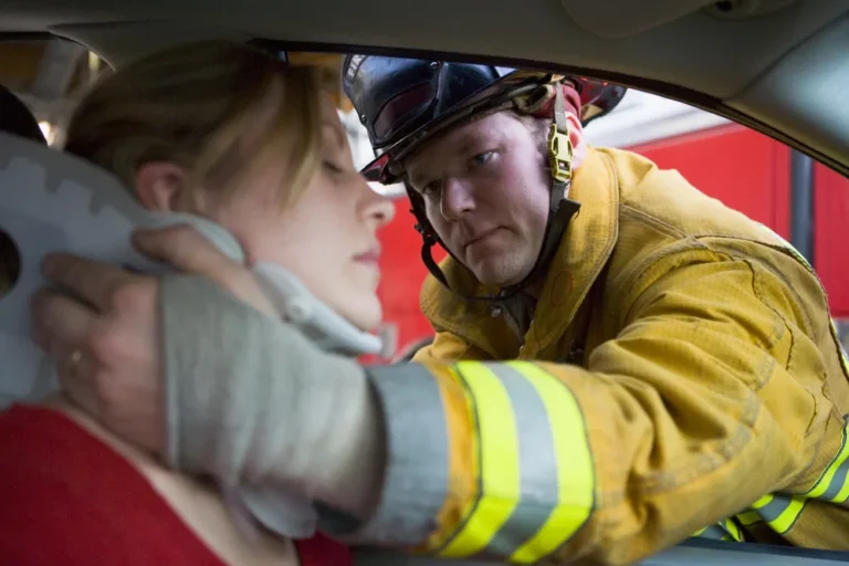 Firefighter supporting a woman’s neck with a cervical collar after a car accident, a common cause of whiplash