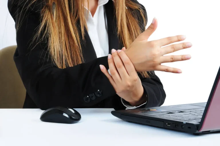 Office worker at a laptop holding her wrist, showing how repeated typing may strain the wrist