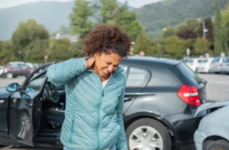 Woman holding her neck in pain beside her car after a rear-end collision, a common cause of whiplash in Canton, OH